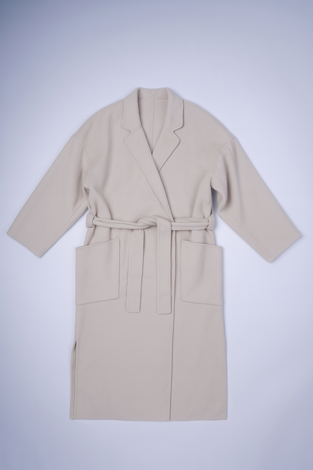 Cream longline coat with classic lapel, patch pockets, and relaxed fit, perfect for cozy layering and elegant style.