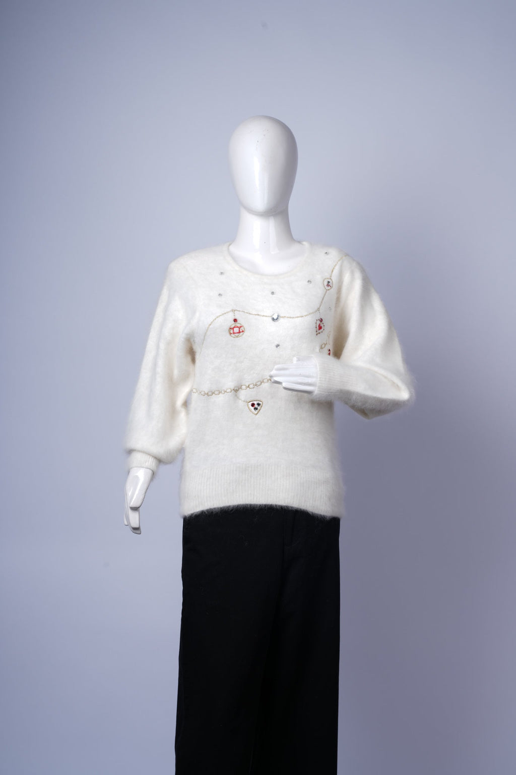 women's stylish cream sweater with decorative chains, pearls, and charms.
