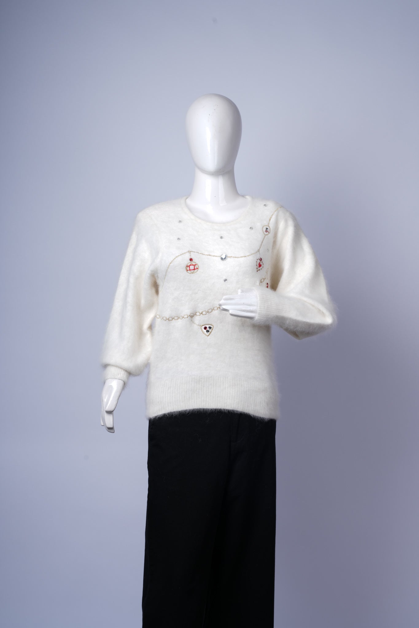 women's stylish cream sweater with decorative chains, pearls, and charms.